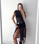 Vestido largo de encaje negro con aberturas laterales, corte ajustado y mangas cortas. Incluye un cinturón con apliques metálicos.