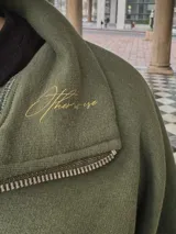 Buzo verde militar de felpa con frisa gruesa, corte boxy, medio cierre con cremallera y estampado minimalista con la frase "The Wise Club Exclusive Members".
