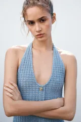 Minivestido celeste de tejido elástico con textura, cuello halter, escote en V, bolsillos simulados y cierre frontal con botones metálicos.