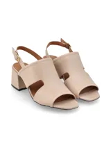 Sandalia de cuero color beige con punta abierta, talón descubierto y tira con hebilla ajustable. Presenta un diseño con aberturas laterales y un tacón bloque bajo.