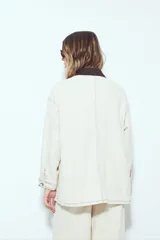 Sobrecamisa tipo barn jacket color negro, de algodón con elastano, con silueta relajada y estructura firme. Presenta cierre frontal con botones metálicos, cuello marrón, bolsillos aplicados y pespuntes visibles en color marrón.