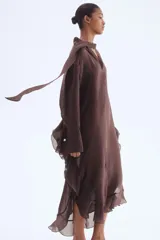 Vestido túnica largo color marrón oscuro, de tejido liviano, con cuello en V con lazos, mangas largas con puños abotonados y volados en mangas, laterales y ruedo.