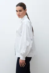 Camisa blanca de manga larga con puños fruncidos y cuello abotonado, corte holgado.