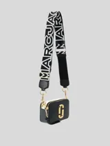 Bolso cruzado Marc Jacobs modelo The Snapshot, color camel, con herrajes dorados y correa ancha intercambiable con texto.