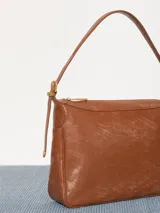 Cartera hobo color marrón confeccionada en cuero vacuno flor, con acceso mediante cierre superior y correa regulable con hebillas metálicas.