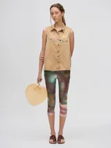 Camisa sin mangas de denim liviano color camel, con cuello camisero y botones frontales. Presenta bordados temáticos marinos en el pecho, incluyendo un sol, olas, una gaviota y vida marina.