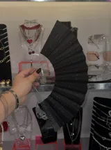 Abanico plegable negro con glitter plateado y varillas de plástico transparente.