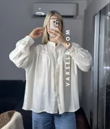 Camisa blanca de mangas largas con detalles de encaje en el cuello y en el frente.