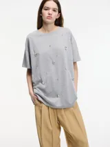 Camiseta gris de algodón con cuello redondo y manga corta. Presenta apliques de brillantes en el frente.
