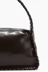 Cartera pequeña color marrón oscuro, de tejido revestido con tira entrelazada en los bordes. Tiene cierre superior, correa corta y forro de tafeta.
