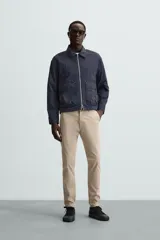 Pantalón chino color beige, corte skinny fit, confeccionado en tejido con mezcla de algodón y elasticidad. Cuenta con bolsillos frontales y traseros. Cierre frontal con cremallera y botón.