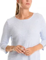 Buzo de tejido suave color beige, con cuello a la base y mangas 3/4 con aplique de botones dorados. Presenta terminación con tajos en los laterales.