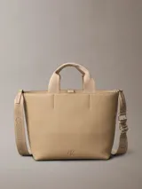 Mini cartera tote Calvin Klein color beige, confeccionada en poliuretano, con doble asa de mano y correa de hombro ajustable extraíble. Incluye cierre con botón a presión y bolsillo interior para tarjeta.