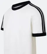 Remera de algodón de corte regular, color blanco hueso, con cuello redondo y ribete negro. Presenta un diseño de doble raya negra en las mangas y ribetes negros en el cuello y los puños de las mangas.