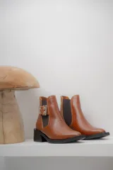 Botines Chelsea color beige con elásticos laterales negros, punta cuadrada, detalle de hebilla lateral y tacón bloque bajo.