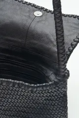 Cartera bandolera negra de cuero vacuno trenzado, con acceso superior con cierre metálico, interior forrado con bolsillos y correa de hombro trenzada.