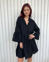 Vestido corto negro con cuello camisero, mangas largas acampanadas y corte holgado.