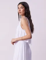 Vestido largo blanco de crepe, con escote redondo y sobrecapa con ruedo de broderie. Corte en la cintura con punto smock.