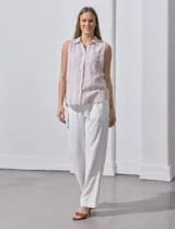 Camisa sin mangas de lino a rayas verticales azules y blancas, con cuello con solapa, escote en V, abertura central con botones y bolsillo en el pecho.