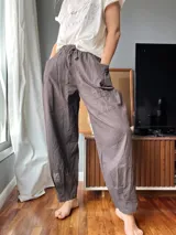 Pantalón de lino color marrón topo, de corte amplio, con cintura elastizada ajustable con cordón, bolsillos laterales y un bolsillo tipo cargo en la pierna derecha.