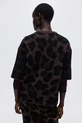 Buzo boxy de punto jacquard suave, con estampado de leopardo en tonos marrón oscuro y negro. Presenta cuello redondo acanalado, hombros caídos y mangas al codo.