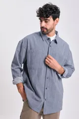 Sobrecamisa de hombre de jean, color azul, con patrón de rayas verticales finas. Presenta cuello camisero, bolsillos frontales con tapa y botones oscuros. Se lleva abierta sobre una remera blanca.