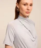 Blusa color gris claro con detalle drapeado en el cuello y mangas cortas.
