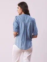 Blusa celeste de lyocell, con cuello a la base, escote en V y botones. Delantera con bolsillo y manga corta con terminación en punto smock.