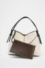 Bolso mini shopper de tejido canvas color crudo con pespuntes en contraste negro. Tiene asas de mano y correa bandolera extraíble. Incluye cartera interior con cremallera dorada.