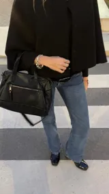 Cartera negra de simil cuero con correa corta y correa larga ajustable. Tiene cierre principal, bolsillos interiores y exteriores en la parte delantera y trasera.