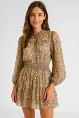 Vestido corto color beige con estampado floral en tonos marrones y azules. Tiene cuello mao, mangas largas abullonadas con puños elásticos, corte holgado, cintura elastizada y falda con volados.