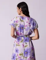 Vestido midi de gasa estampada con flores violetas y verdes, escote en V, abertura central con botones, cintura con lazo de ajuste y forro interno a tono.