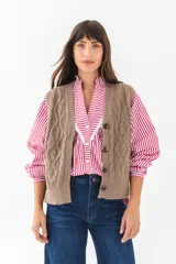 Chaleco de punto color marrón claro con diseño trenzado, cuello en V y cierre frontal con botones. Sin mangas.