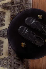 Sandalias chatitas negras de cuero con múltiples tiras finas y tachas doradas.