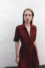 Vestido midi camisero color ladrillo, confeccionado en popelina de algodón. Presenta cuello solapa, manga corta con puños abotonados, bolsillos laterales ocultos y bolsillos de parche con solapa en el pecho. Incluye cinturón lazada en el mismo tejido y cierre frontal con botones ocultos.