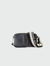 Bandolera Marc Jacobs modelo The Snapshot, de cuero color gris con detalles en beige y herrajes dorados. Presenta correa de tela con el logo de la marca y doble compartimento con cierre.