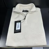 Buzo de punto color crudo, con cuello polo y cierre metálico a mitad del frente.