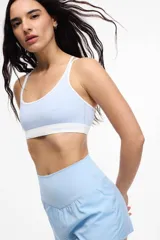 Top deportivo celeste con contorno y tirantes blancos. Presenta copas removibles y el logo de la marca en el contorno inferior.