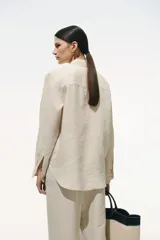 Camisa color crudo de lino liviano, con cuello clásico, botones al frente, canesú de doble capa en la espalda, hombros apenas caídos, mangas largas con puños abotonados, bolsillo superior de parche y bajo levemente redondeado.