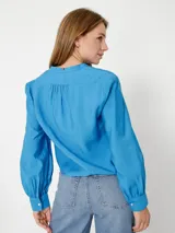 Camisa celeste de corte cropped, sin cuello, con mangas largas abullonadas y puños con botón.