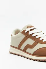 Zapatillas beige con recortes en gamuza de diferentes tonos, cordones y suela irregular blanca con detalle rosa.