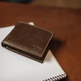 Billetera de cuero marrón con costuras blancas, múltiples ranuras para tarjetas y compartimento para billetes con cierre interno.