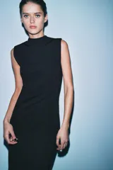 Vestido negro, largo, de cuello perkins y manga sisa, con detalle de espalda descubierta y bajo en línea evasé.