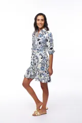 Vestido corto con estampado floral en tonos azules y negros sobre fondo blanco, corte camisero con cuello clásico, mangas 3/4 y falda con volantes.