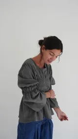 Camisa a cuadros azul y gris con cuello redondo y mangas largas abullonadas. Presenta detalle de fruncido en el frente y puños elásticos.