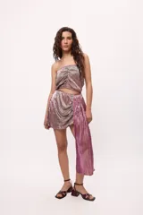 Falda corta color rosa metalizado, con frunces y drapeado lateral que se extiende hasta el tobillo.