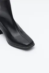 Bota corta de caña elástica color negro, con puntera cuadrada y taco geométrico de altura media. Presenta cierre de cremallera en la parte trasera.