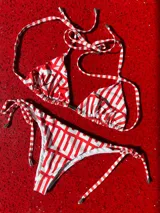 Conjunto de bikini de lycra suave y resistente, con estampado gráfico en tonos rojos y blancos. La parte superior es un top triángulo con tirantes finos y la parte inferior es una bombacha con tiras laterales ajustables.