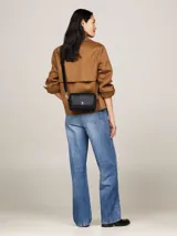 Bandolera Tommy Hilfiger negra con correa ajustable y logo metálico dorado en el frente.