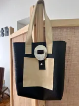 Bolso tote negro con textura símil cuero de cocodrilo, con bolsillo frontal marrón y herrajes plateados.